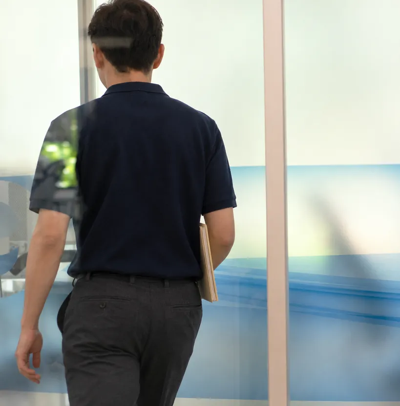 A person in a navy outfit is seen from behind through a glass window. The setting appears calm, with soft light and minimalistic decor in blue tones.